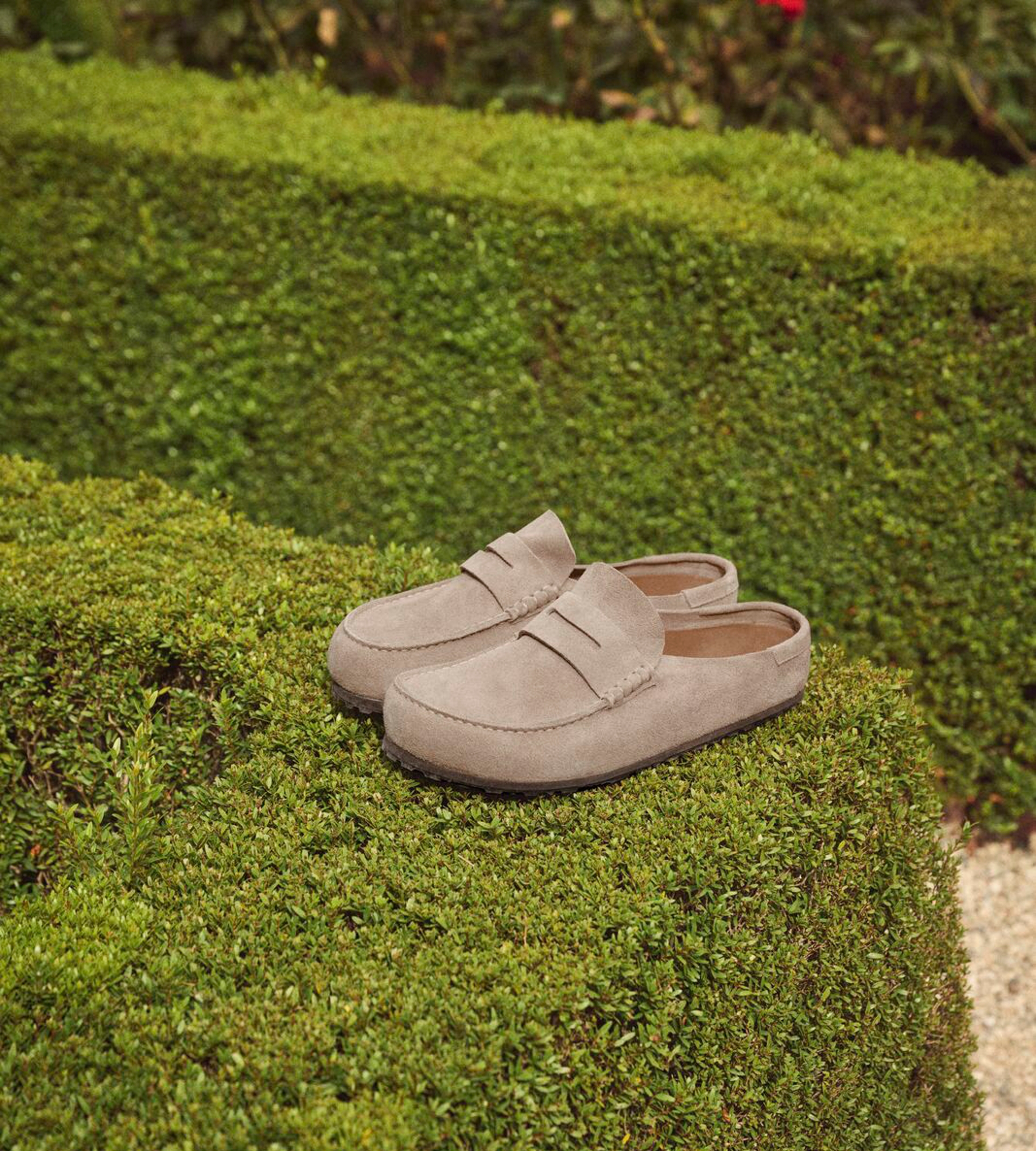 Close up of the birkenstock naples clog sitting on a bright green hedge.