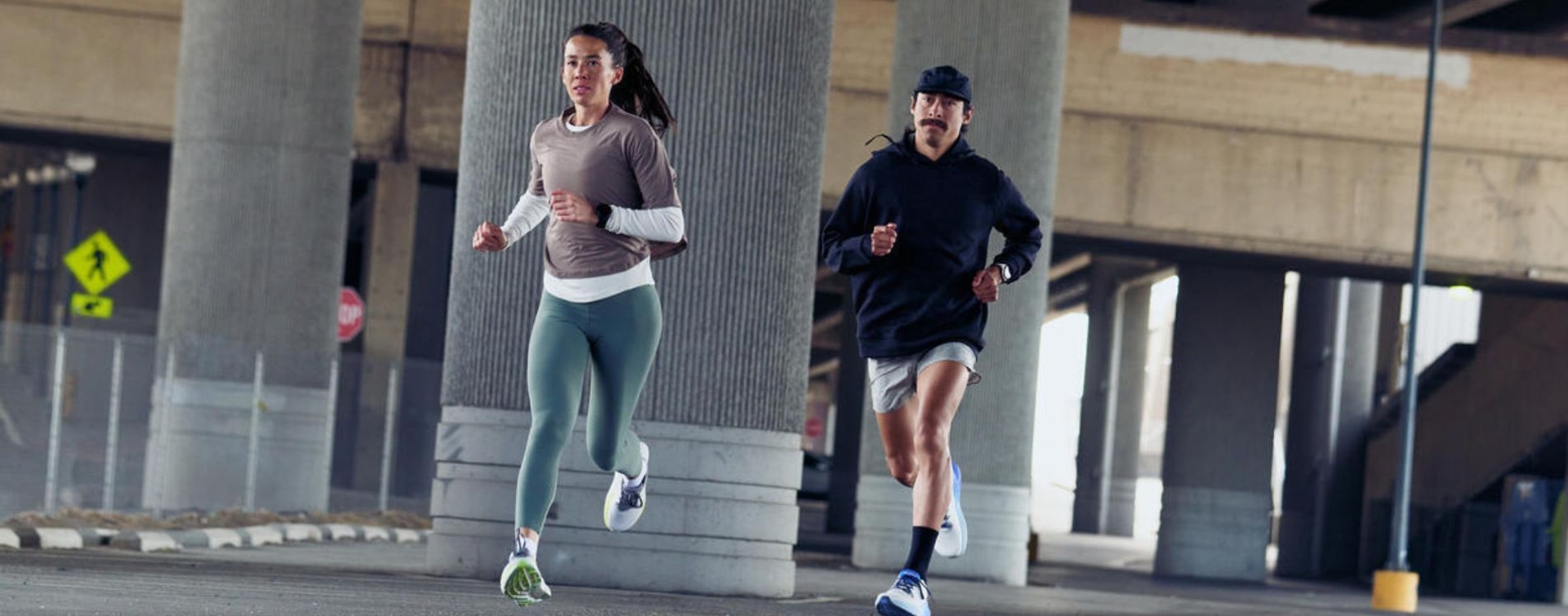 A man and woman running in Altra shoes through an urban landscape