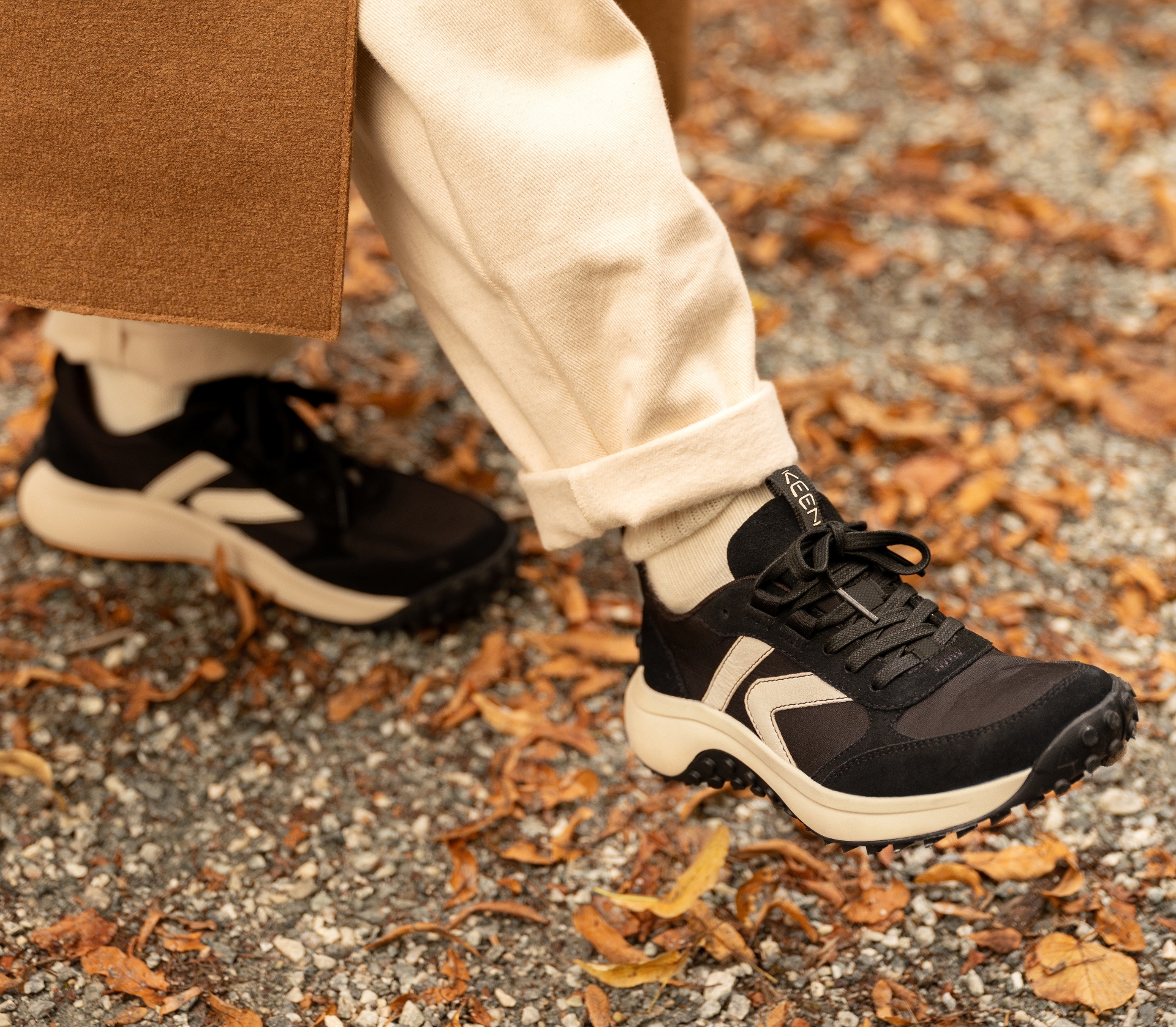 close up of a woman on a path walking over fall leaves in black and white keen sneakers 