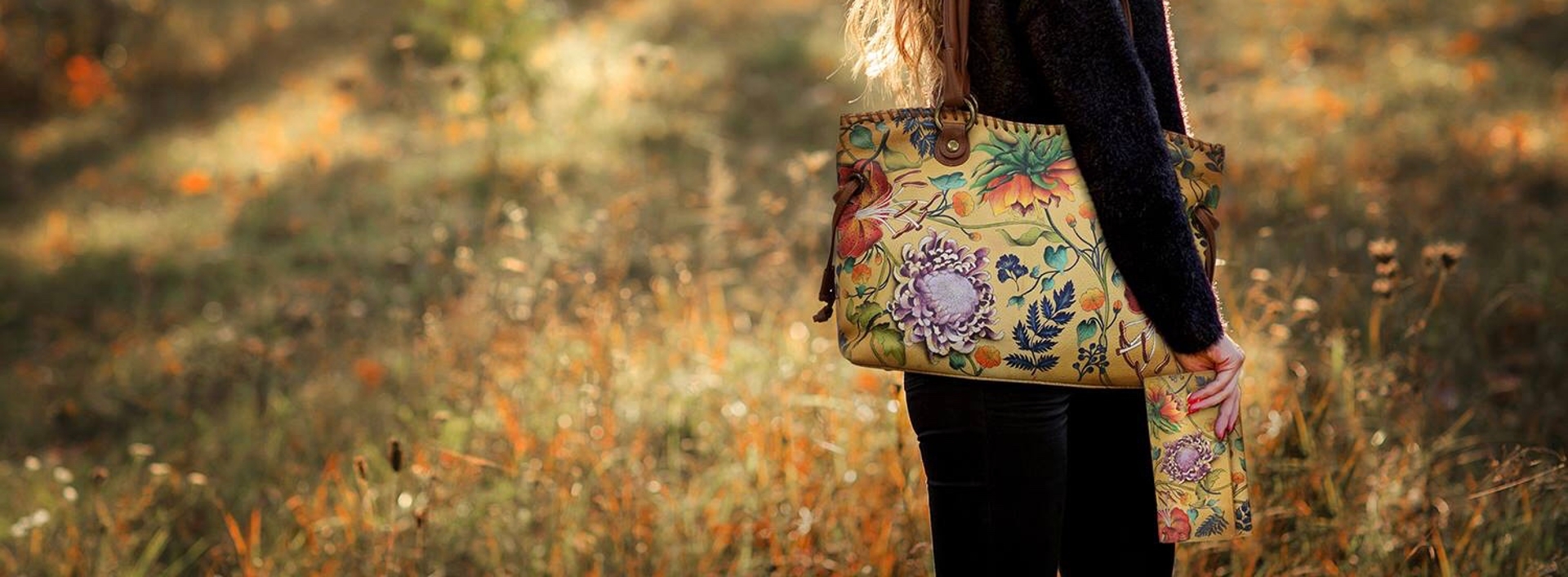 Woman with floral print handbag and matching accordion wallet standing in a field