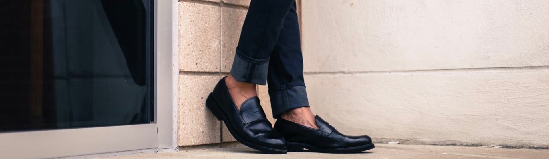 Feet in black oxfords resting against brick wall