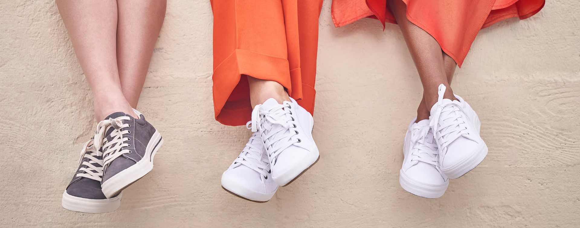 Close up shot of 3 ladies feet dangling over a brick wall wearing Taos Sneakers. 