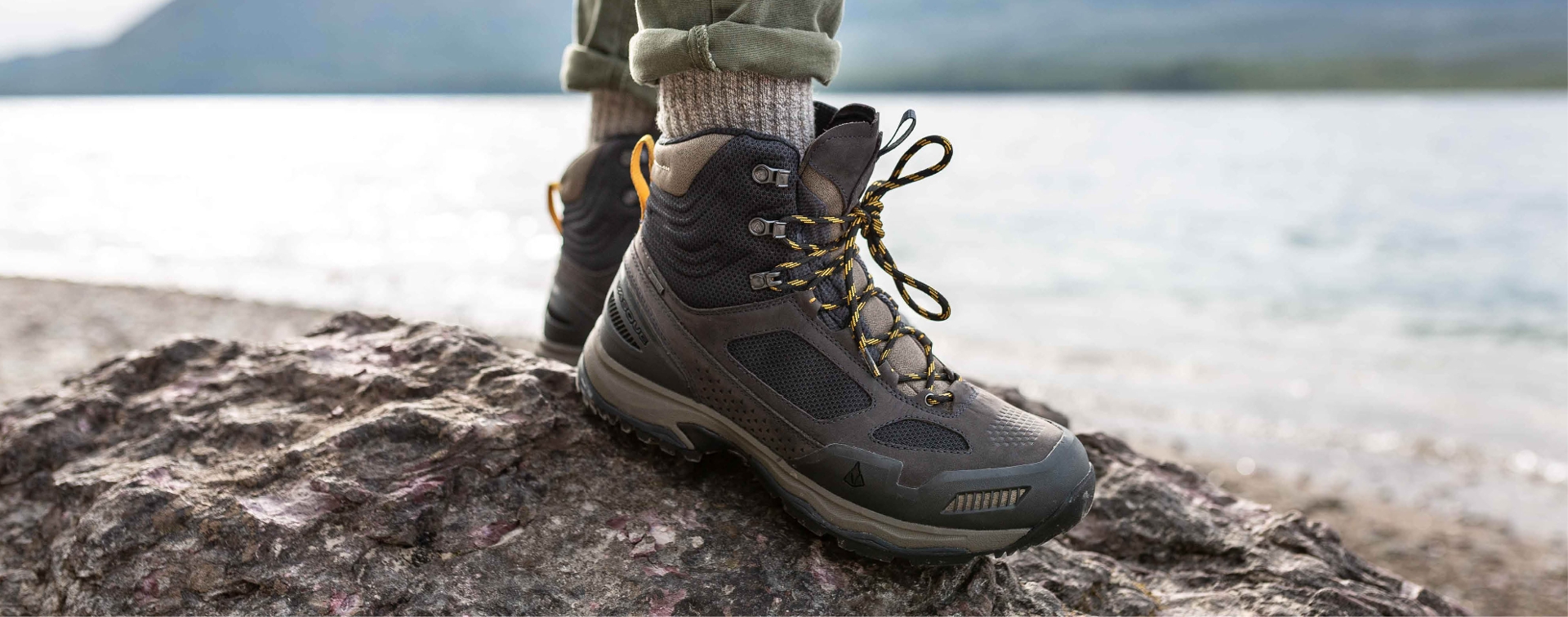 close up of guy in green pants standing on a rock in boots.