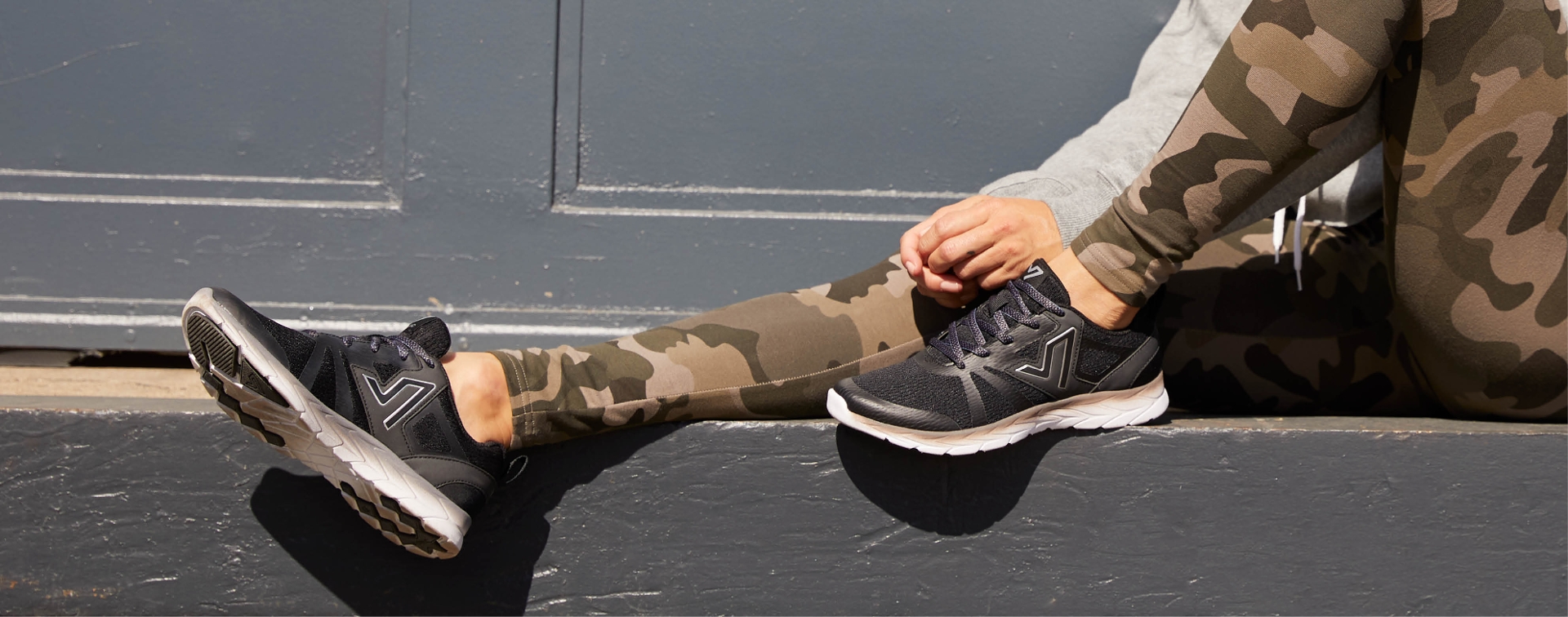 girl sitting on a wall with legs out wearing camo pants an a black pair of shoes in 